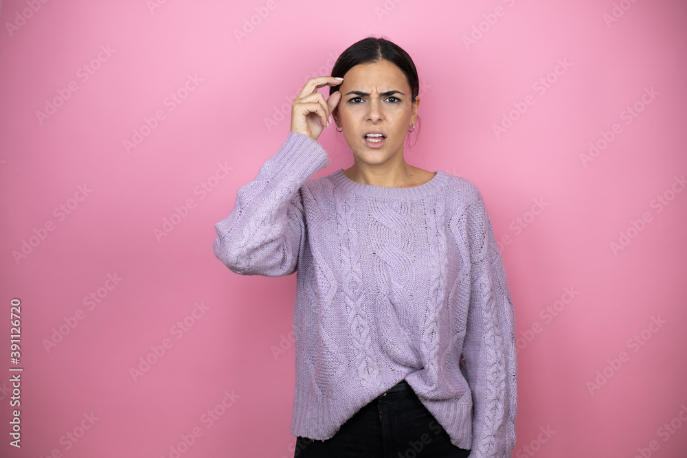 Fototapeta premium Beautiful woman wearing a casual violet sweater over pink background confused and wonder about question. Uncertain with doubt, thinking with hand on head
