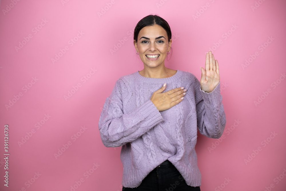 Fototapeta premium Beautiful woman wearing a casual violet sweater over pink background smiling swearing with hand on chest and fingers up, making a loyalty promise oath
