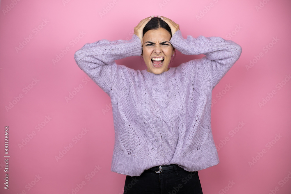 Beautiful woman wearing a casual violet sweater over pink background suffering from headache desperate and stressed because pain and migraine with her hands on head Beautiful woman wearing a casual violet sweater over pink background suffering from headache desperate and stressed because pain and migraine with her hands on head