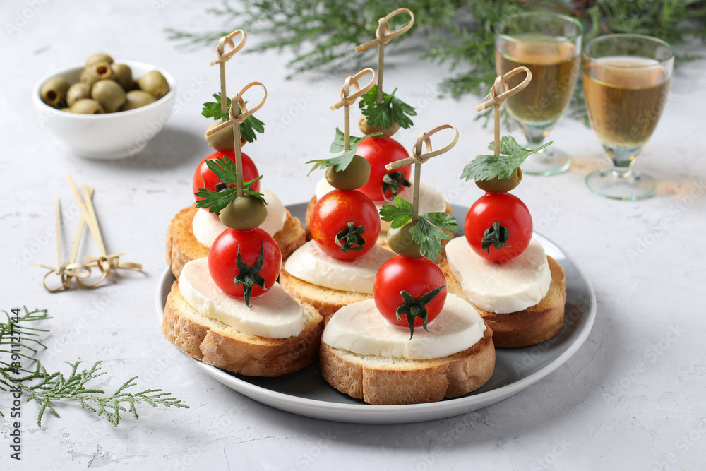 Canapes of mozzarella, cherry tomatoes, green olives, parsley on croutons of white bread on gray background. Festive New Year snack. Closeup Canapes of mozzarella, cherry tomatoes, green olives, parsley on croutons of white bread on gray background. Festive New Year snack. Closeup