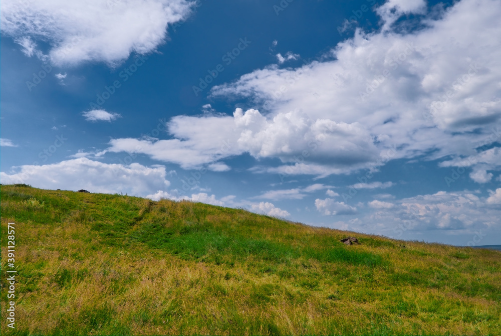Summer landscape mountain slope with beautiful grass against the blue sky and cumulus white clouds.