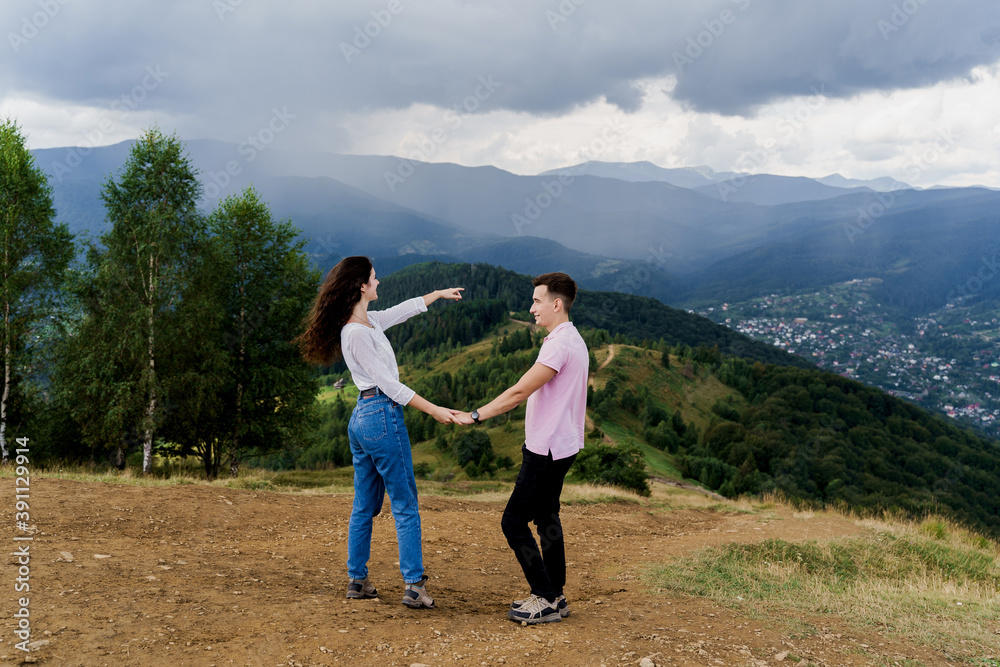 Girl points her boyfriend at rain far away. Couple looking at the mountain hills before raining. Feeling freedom together in Karpathian mountains. Tourism travelling in Ukraine