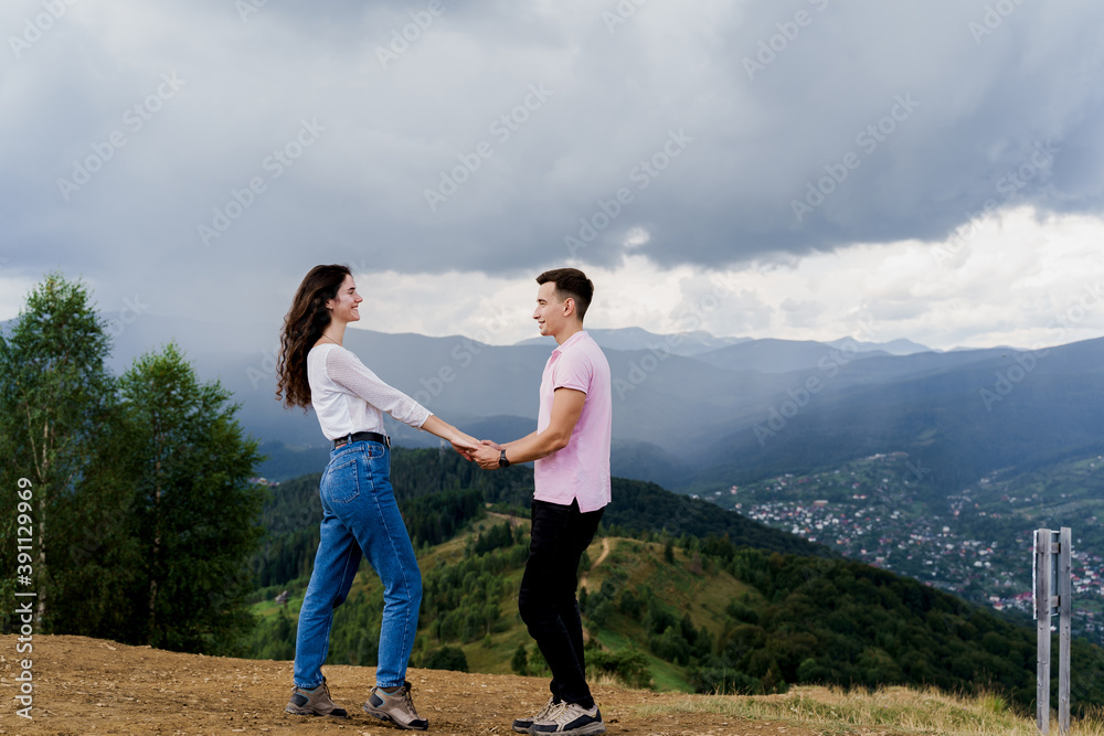 Couple looking to each other at the mountain hills before raining. Feeling freedom together in Karpathian mountains. Tourism travelling in Ukraine. Couple looking to each other at the mountain hills before raining. Feeling freedom together in Karpathian mountains. Tourism travelling in Ukraine.