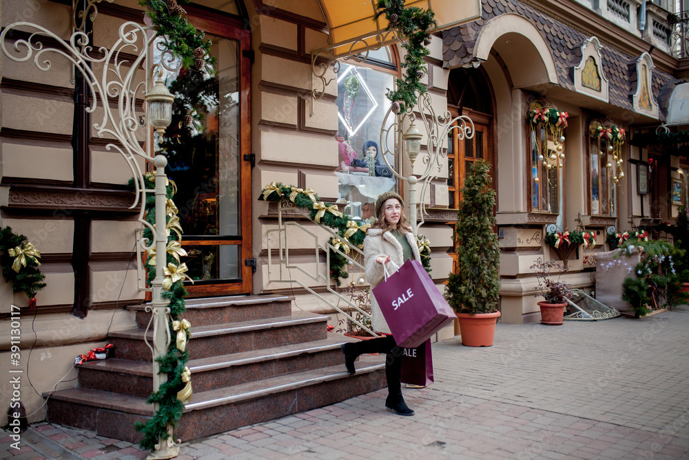 Happy girl holds paperbags with symbol of sale in the stores with sales at Christmas, around the city. Concept of shopping, holidays, happiness, Christmas Sales. Happy girl holds paperbags with symbol of sale in the stores with sales at Christmas, around the city. Concept of shopping, holidays, happiness, Christmas Sales.