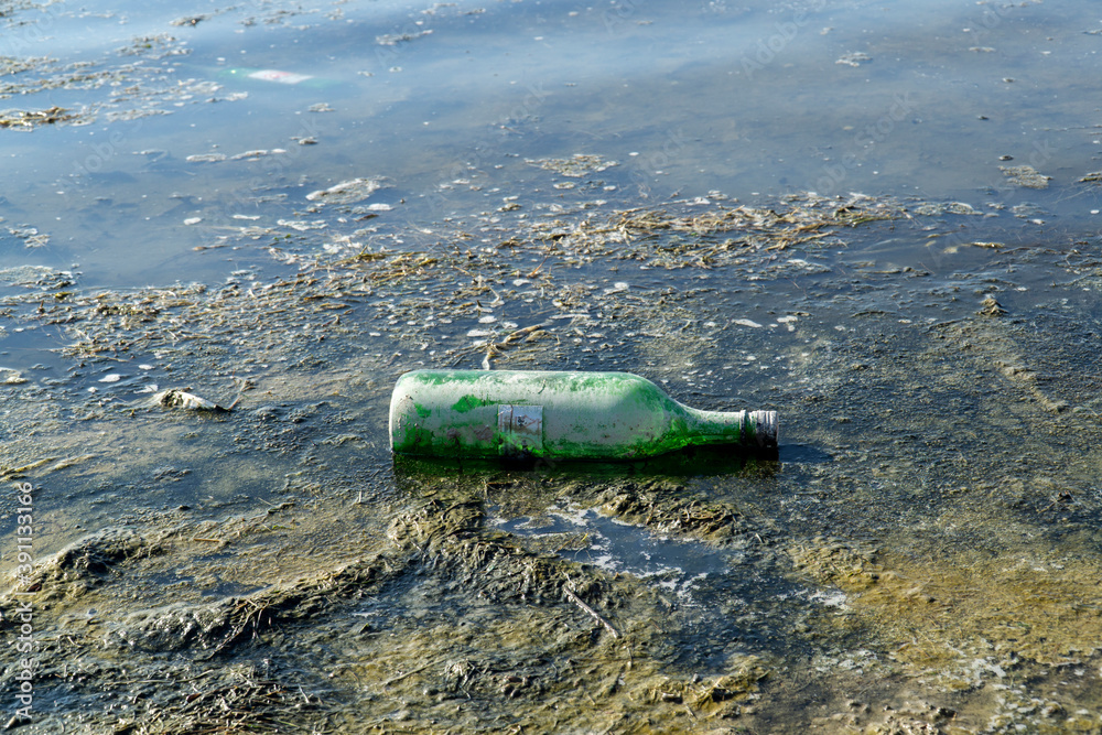 Plastic garbage in the lake , pollution and environment concept. A green bottle by the lake, Plastic garbage in the lake , pollution and environment concept. A green bottle by the lake,