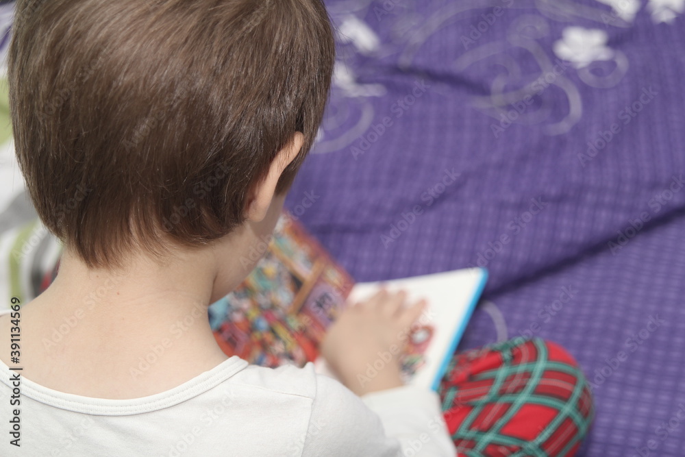 The boy sits in bed and looks at a book before going to bed. The boy sits in bed and looks at a book before going to bed.