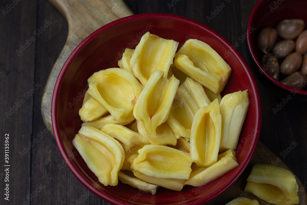Buah Nangka or Jackfruit, one of tropical fruits popular in Indonesia. Cut into half on red bowl and the seeds at behind. Dark wooden background. Buah Nangka or Jackfruit, one of tropical fruits popular in Indonesia. Cut into half on red bowl and the seeds at behind. Dark wooden background.