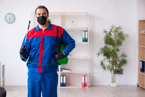 Young male contractor disinfecting office