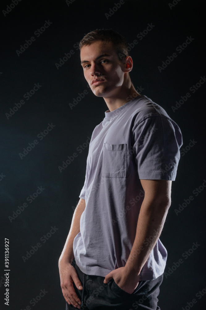 Portrait of a handsome young man wearing a gray t-shirt and black pants poses on black background in a studio Portrait of a handsome young man wearing a gray t-shirt and black pants poses on black background in a studio