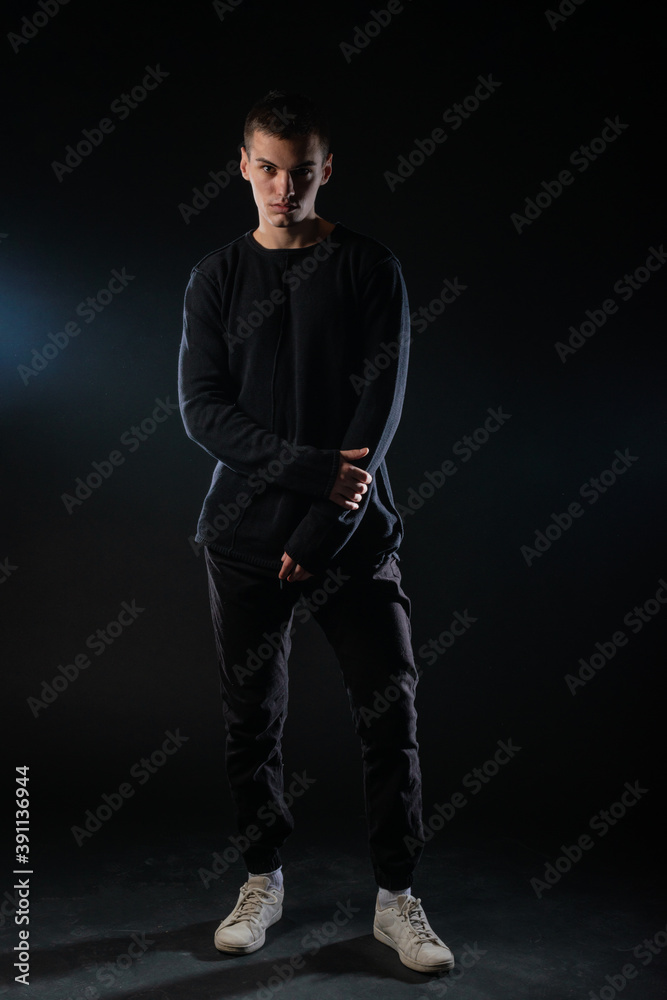 Full-length picture of an attractive sexy young male model posing isolated on a black background and wearing black blouse and black pants. Full-length picture of an attractive sexy young male model posing isolated on a black background and wearing black blouse and black pants.