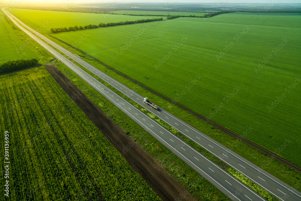blue truck driving on asphalt road along the green fields. seen from the air. Aerial view landscape. drone photography.  cargo delivery. Sunset time