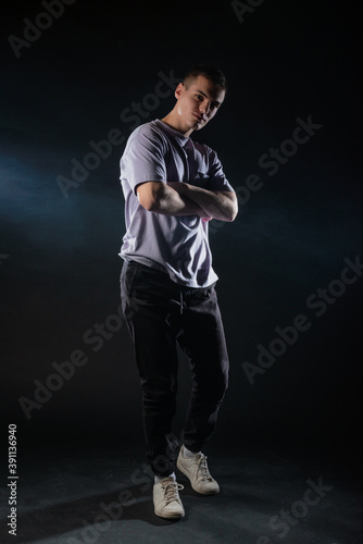 Handsome young man wearing a gray t-shirt and black pants poses on black background in a studio