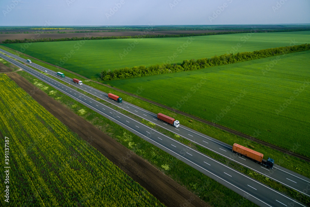 cargo delivery and transportation. serval trucks whith container  driving on asphalt road along the green fields. seen from the air. Aerial view landscape. drone photography. Left side traffic