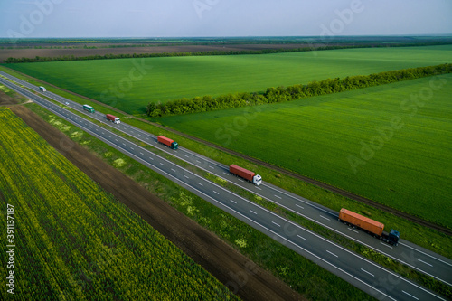cargo delivery and transportation. serval trucks whith container driving on asphalt road along the green fields. seen from the air. Aerial view landscape. drone photography. Left side traffic