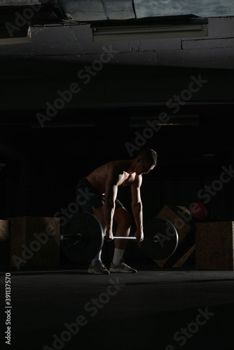  Silhouette of a fit strong shirtless athlete doing squats. Weight lifting workout concept.