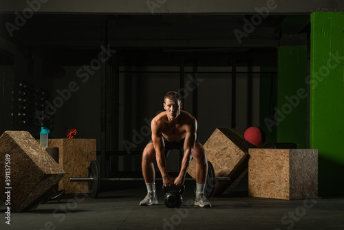 Full-length photo of a handsome man with a naked torso exercising with a kettlebell on a dark background