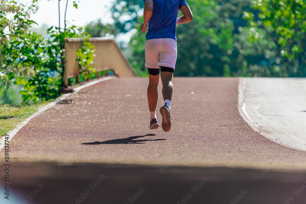 Athletic young man running on the race track in a sports park