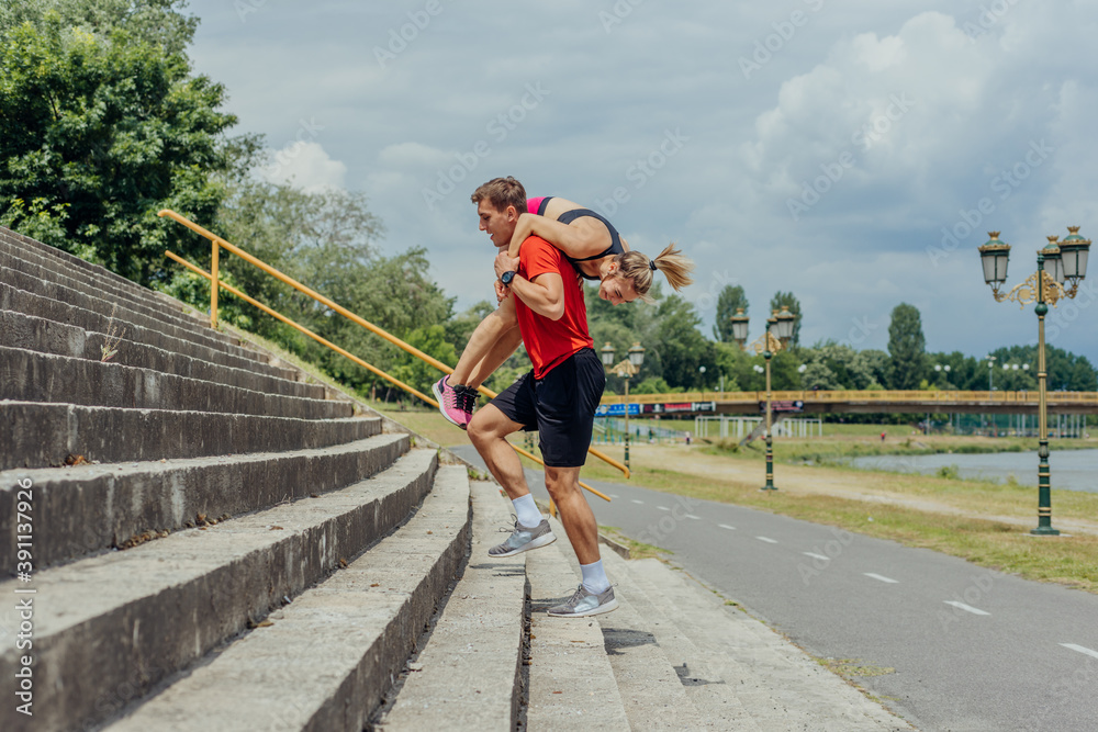 Male athlete carrying his female workout partner on his shoulders while running up the stairs