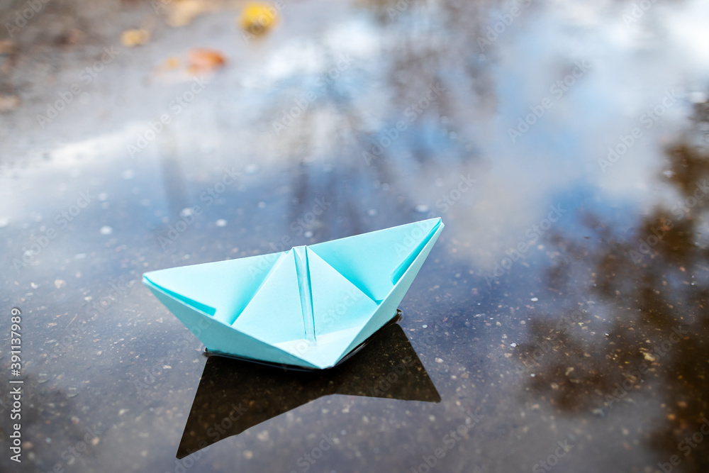 one blue paper ship floating on a water surface. outdoors. autumn season. greeting card with copy space. leadership conceptual. freedom concept