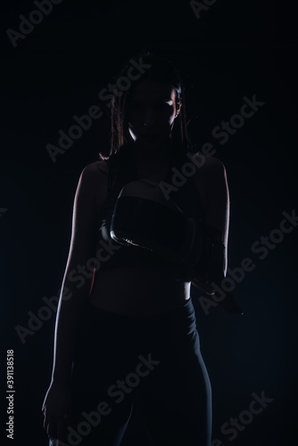 Silhouette portrait of a sexy fit woman posing in dark contrast with boxing gloves