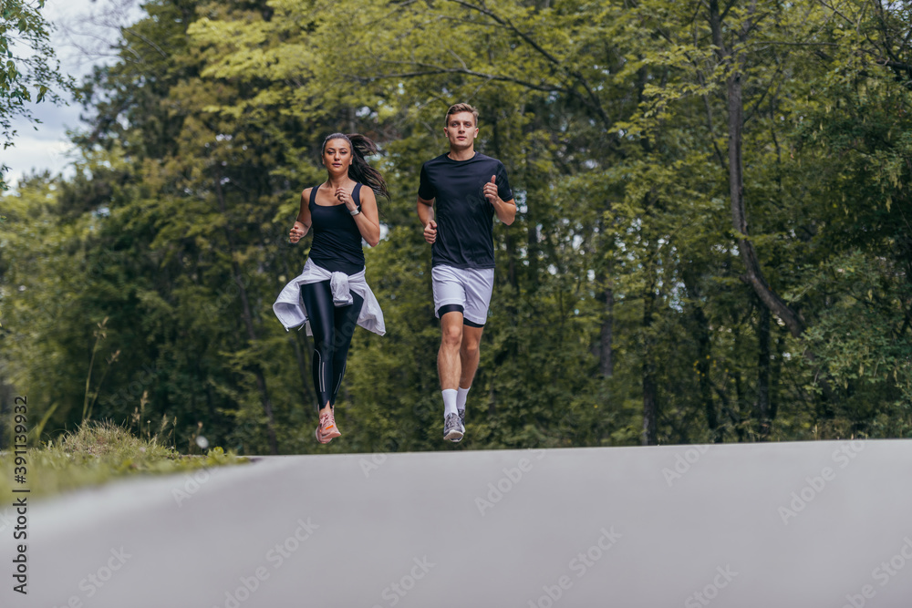 Obraz premium Young fit couple atheltes running on running road in a forest.