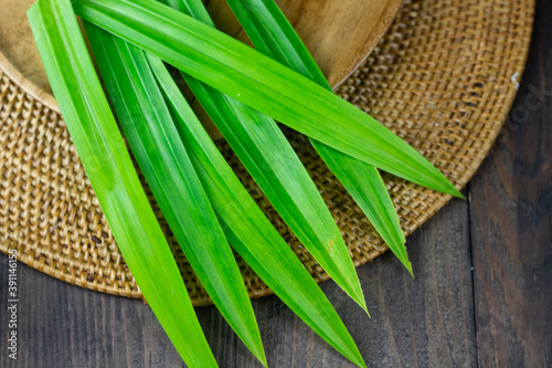 Close up view of pandan leaves or pandanus leaves on wooden brown plate. Pandan leaves usually use as food coloring with aromatic smell. Dark wooden background.  photo