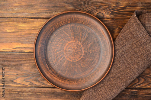 brown empty clay plate with napkin on a wooden background top view, mock up, copy space