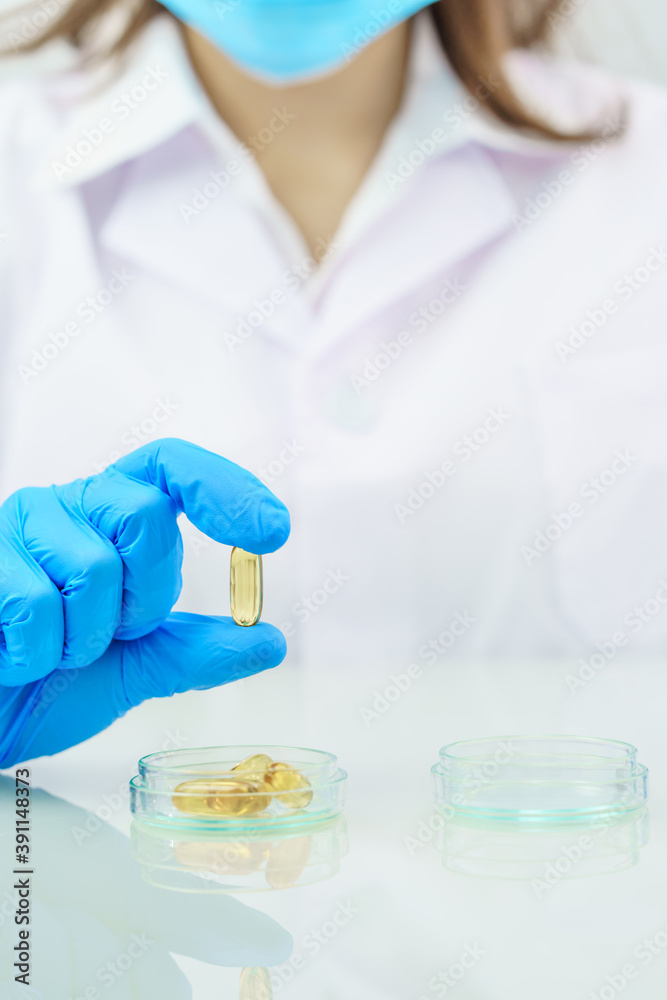 Scientist hands putting in nitrile blue latex gloves holding Omega 3 capsule in labcoat Scientist hands putting in nitrile blue latex gloves holding Omega 3 capsule in labcoat