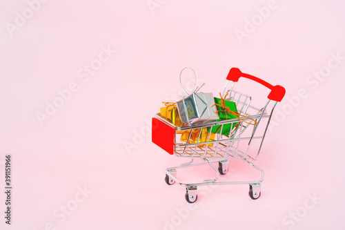 small gift boxes in miniature shopping cart on sweet pink background