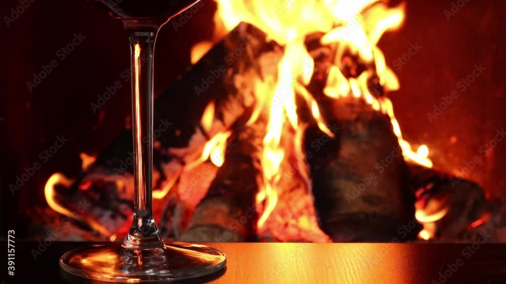 Glass of red wine and birch logs of firewood in burning fire in fireplace, close-up Glass of red wine and birch logs of firewood in burning fire in fireplace, close-up