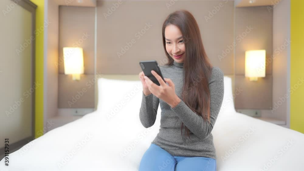 Attractive girl using a mobile phone and surfing on the internet or chekcing social media while sitting on a white mattress of her bed. Attractive girl using a mobile phone and surfing on the internet or chekcing social media while sitting on a white mattress of her bed.