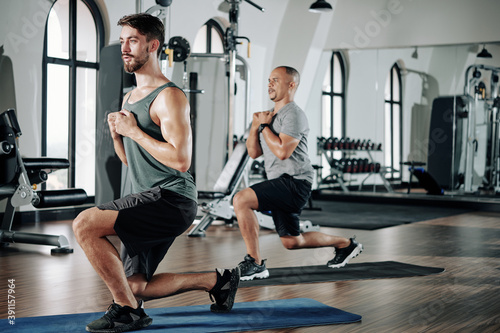 Fit men keeping hands on their chest when doing deep lunges in gym