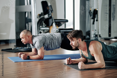 Concentrated serious fit men standing in plank position on gym floor