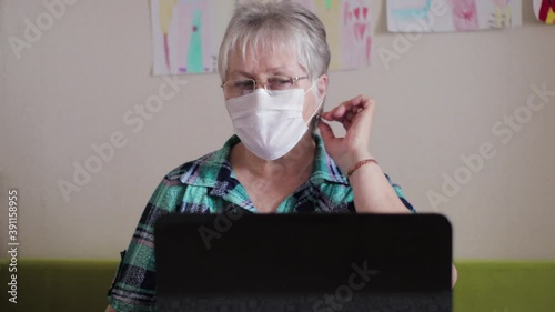 Older woman in protective medical mask at a laptop. Woman talking on the Internet during quarantine