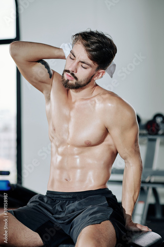 Shirtless sensual young fit man wiping sweat after working out in gym