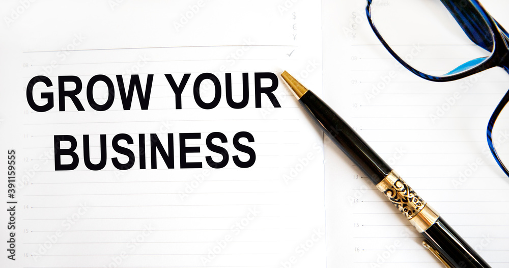 In the notebook the text GROW YOUR BUSINESS, a row pen, glasses. In the notebook the text GROW YOUR BUSINESS, a row pen, glasses.