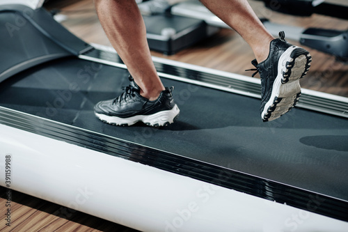 Close-up image of fit man in sneakers running fast on treadmill in gym in the morning © DragonImages