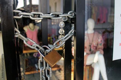 Closed clothing store with padlock and chains in the door. Mannequins and some women clothes in the background. 
