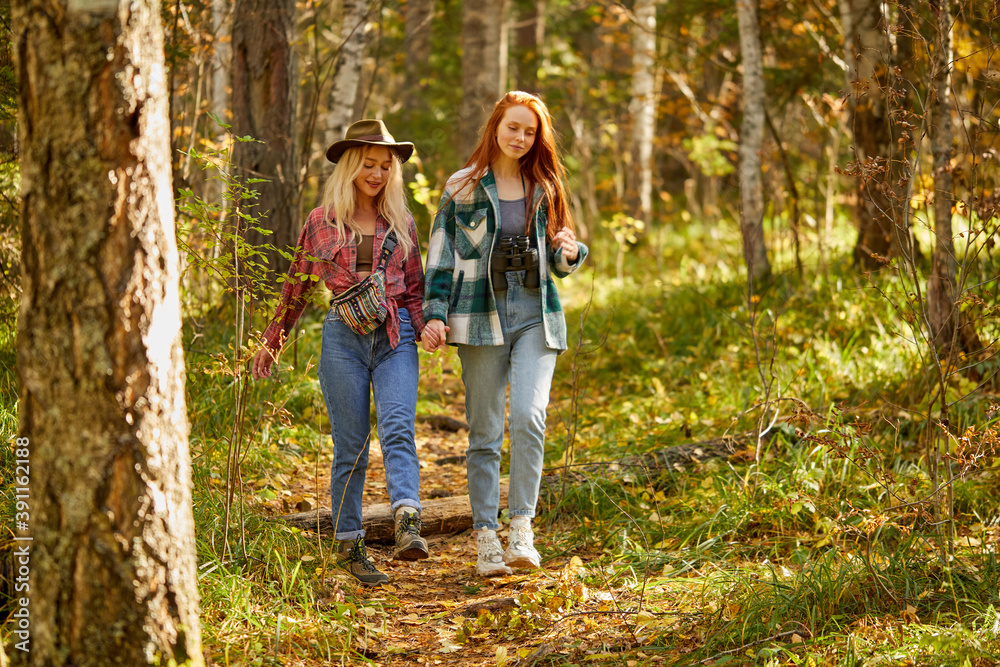 two friendly women hiking together, go forward in the forest. young and beautiful travellers in the nature