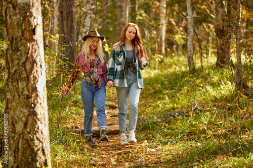 two friendly women hiking together, go forward in the forest. young and beautiful travellers in the nature