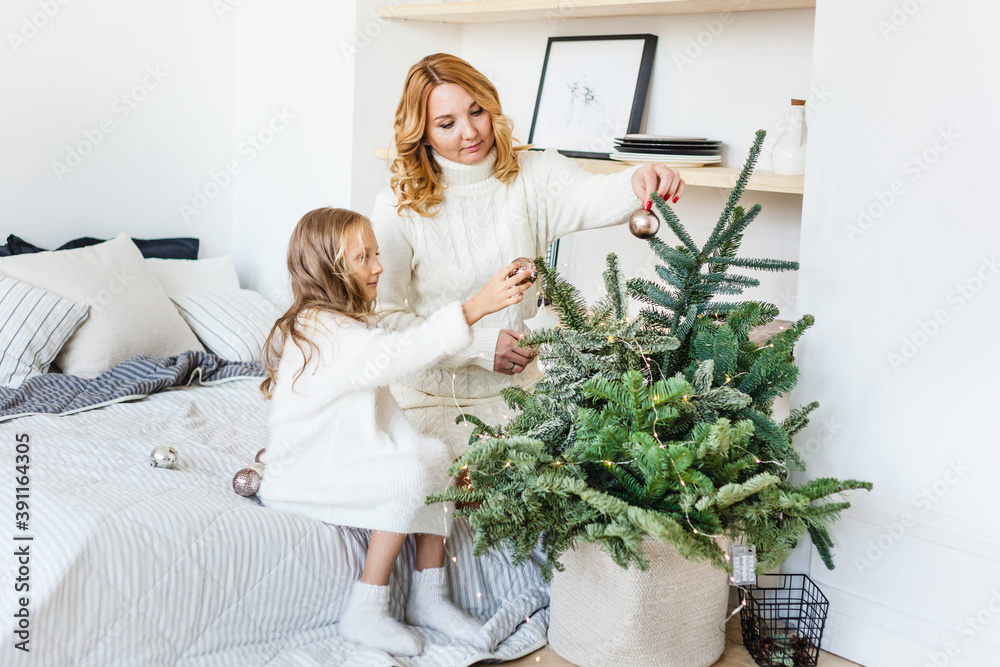 Mom and daughter blonde hair and white sweaters lie on the bed, light up, say toys for Christmas and new year tree, Christmas tree decoration Mom and daughter blonde hair and white sweaters lie on the bed, light up, say toys for Christmas and new year tree, Christmas tree decoration