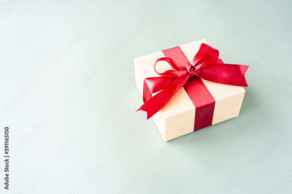stylish square beige box with red festive satin ribbon on pastel blue background with space for text. Festive ready made layout, selective focus stylish square beige box with red festive satin ribbon on pastel blue background with space for text. Festive ready made layout, selective focus