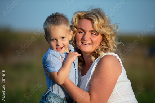 Happy mom with her son outdoors. Blonde European style woman hugs little boy.