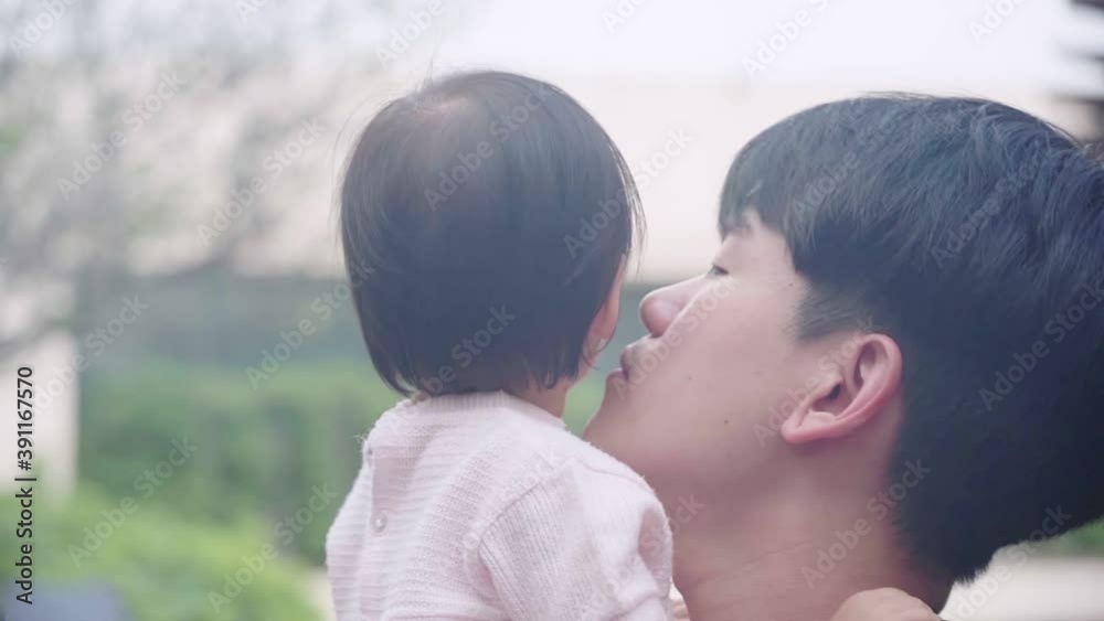 Head shot of young Asian father holding and kissing his adorable cute baby girl, small kid child care parenting, standing outside shot, Family member bonding, daddy lift baby up rest on his shoulder