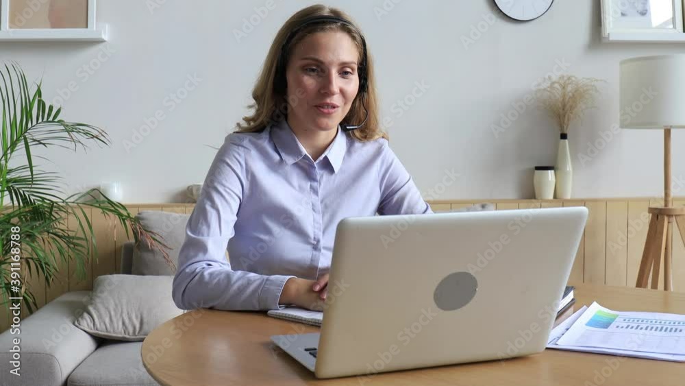 Young call operator businesswoman wears headset customer service manager looking and speaking to webcam on laptop communicating in distance remote chat. Young call operator businesswoman wears headset customer service manager looking and speaking to webcam on laptop communicating in distance remote chat.