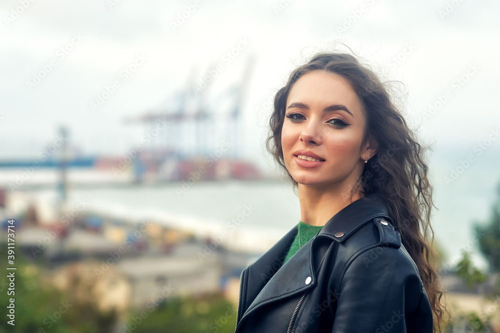 Portrait of a young beautiful girl with curly hair in a fashionable leather jacket outdoors Portrait of a young beautiful girl with curly hair in a fashionable leather jacket outdoors