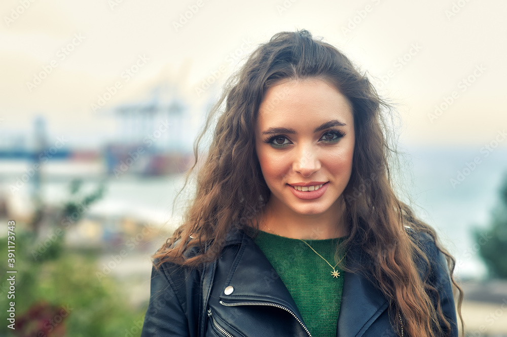 Portrait of a young beautiful girl with curly hair in a fashionable leather jacket outdoors Portrait of a young beautiful girl with curly hair in a fashionable leather jacket outdoors