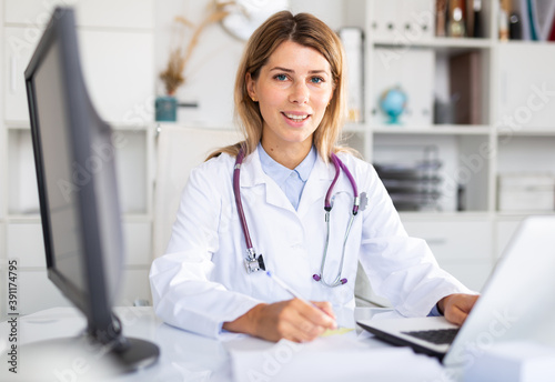 Woman doctor sitting at workplace with computer in her office