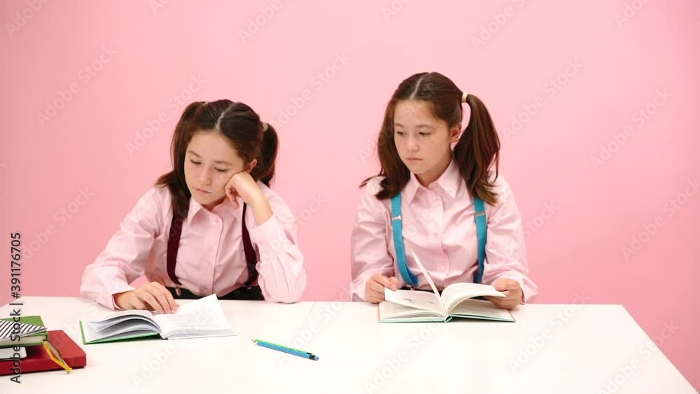 Bored twin schoolgirls sitting behind school desk. One making hand binoculars Bored twin schoolgirls sitting behind school desk. One making hand binoculars