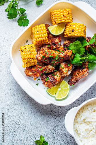 Barbecue chicken wings served with grilled corn and rice in white dish, gray background.